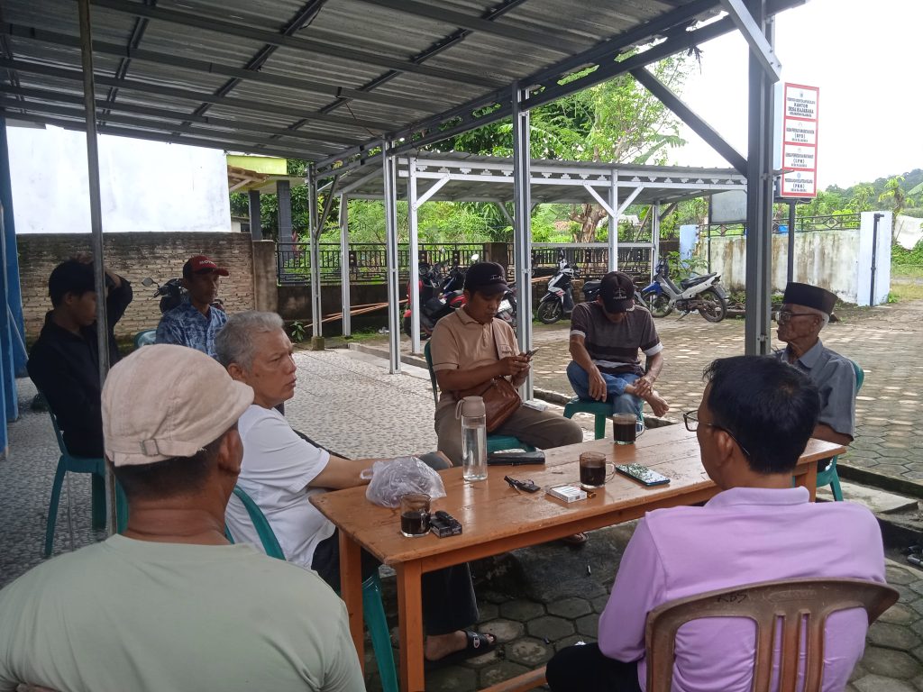 Beberapa laki-laki sedang duduk berdiskusi di depan kantor Balai Desa 