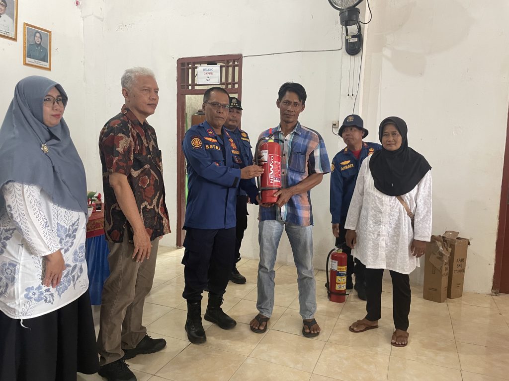 Seorang laki-laki sedang menerima Alat Pemadam Api Ringan dari Seorang pria berseragam pemadam kebakaran