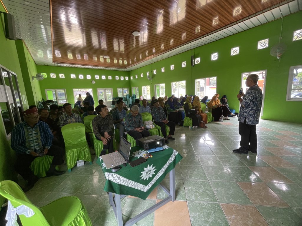 Seorang laki-laki sedang berbicara di hadapan banyak orang yang sedang duduk