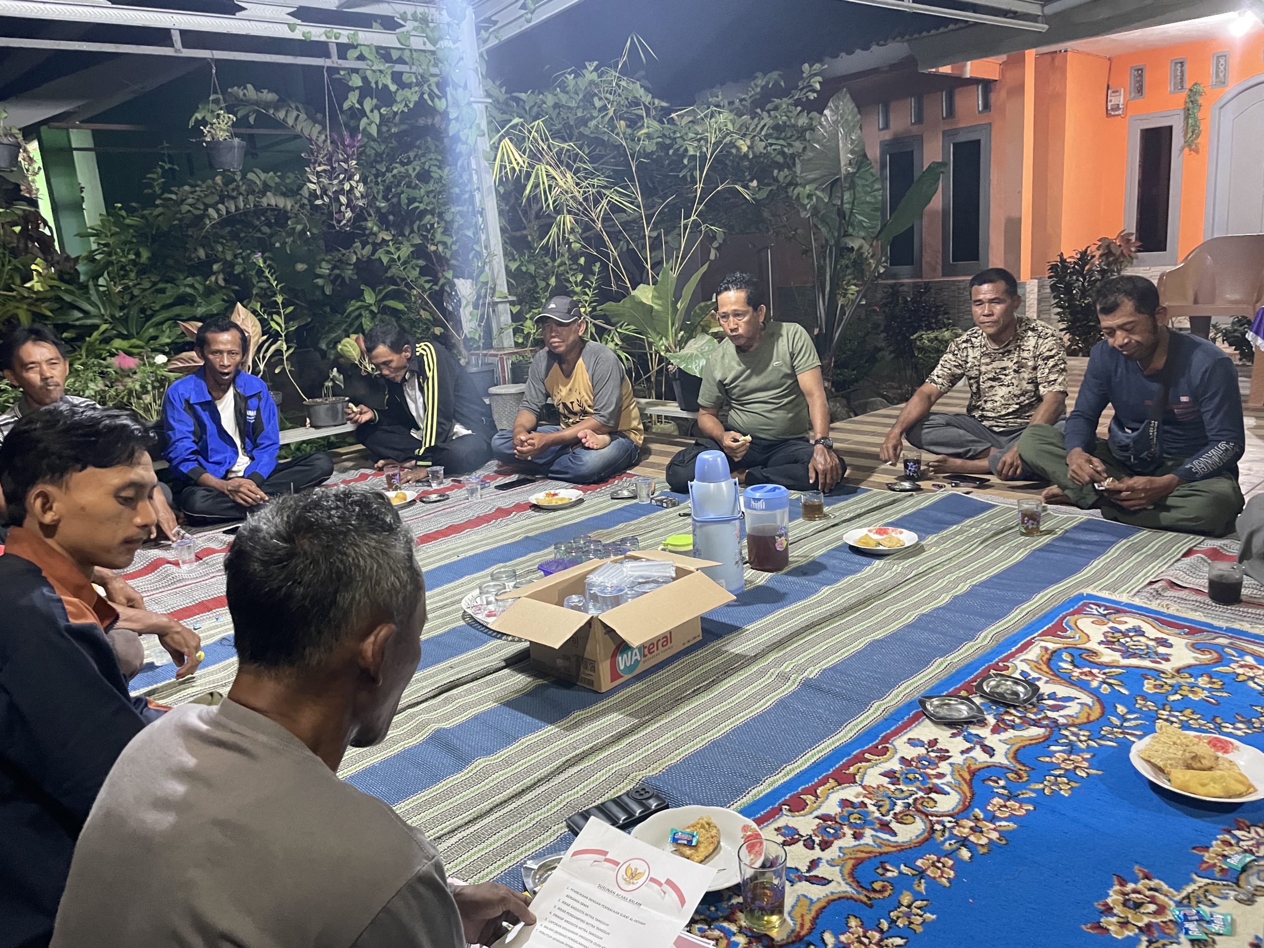 Foto suasana berbagi pengalaman, sejumlah orang duduk bersila melingkar di halaman rumah