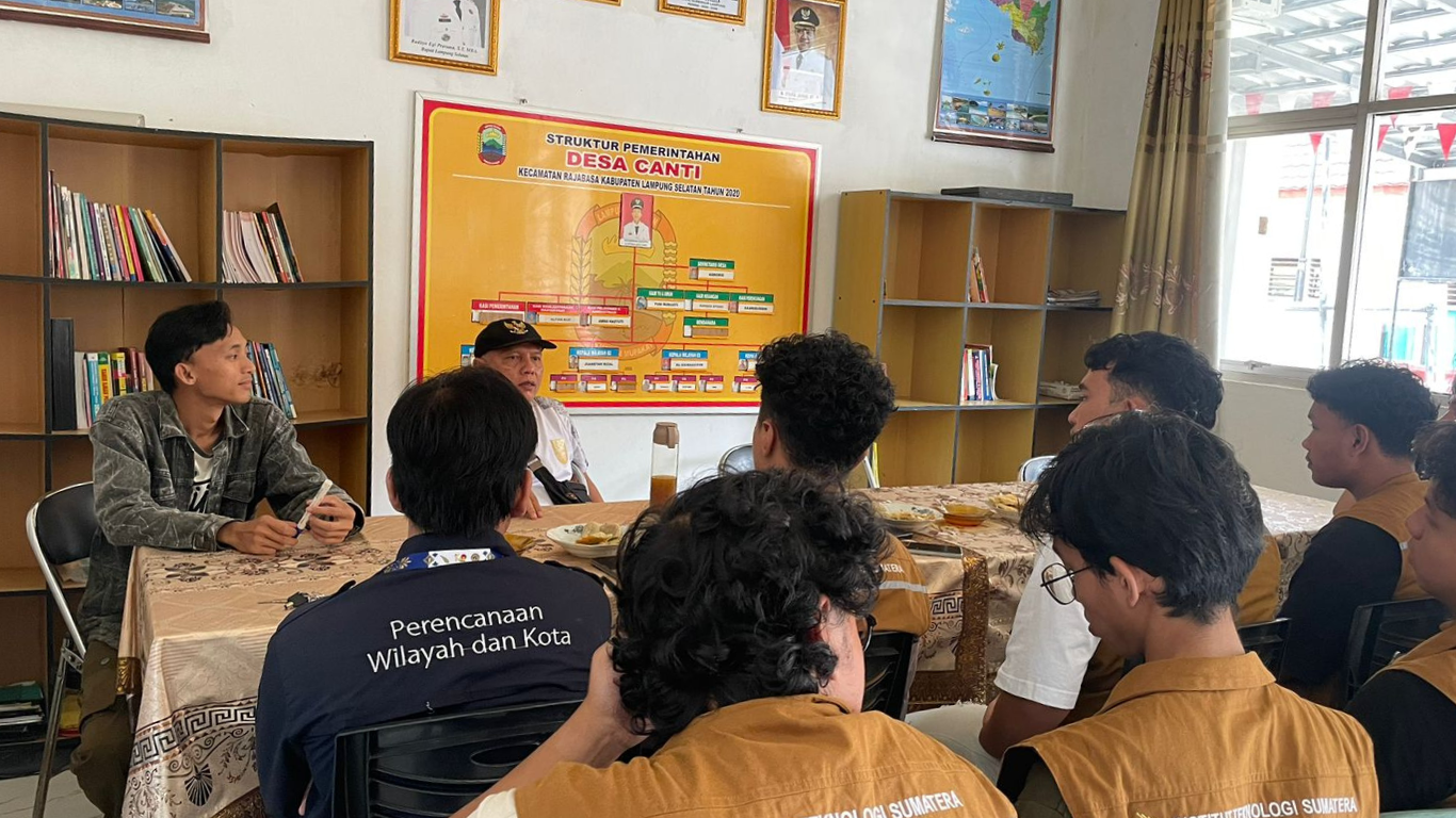 Sejumlah mahasiswa Institut Teknologi Sumatera mengenakan rompi cokelat duduk melingkar mengikuti diskusi bersama aparatur desa di dalam ruang kantor Desa Canti, Lampung Selatan, dengan latar peta wilayah dan struktur pemerintahan desa di dinding.
