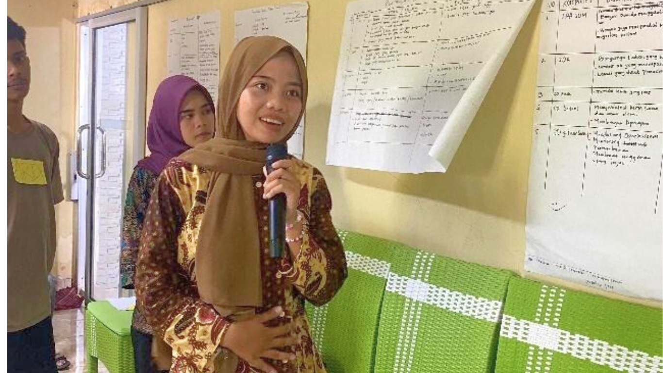 Perempuan berjilbab sedang presentasi dan berbicara dengan microphone