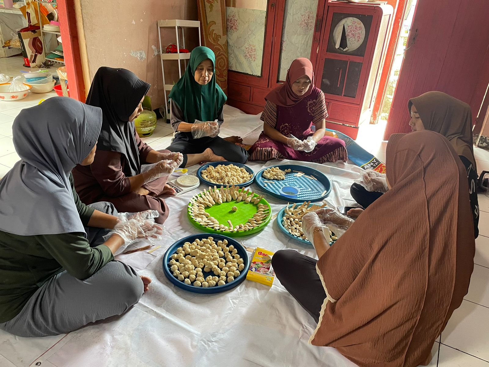 Sekelompok ibu-ibu duduk melingkar dengan tampah-tampah berjejer di tengah berisi adonan frozen food yang siap dibentuk