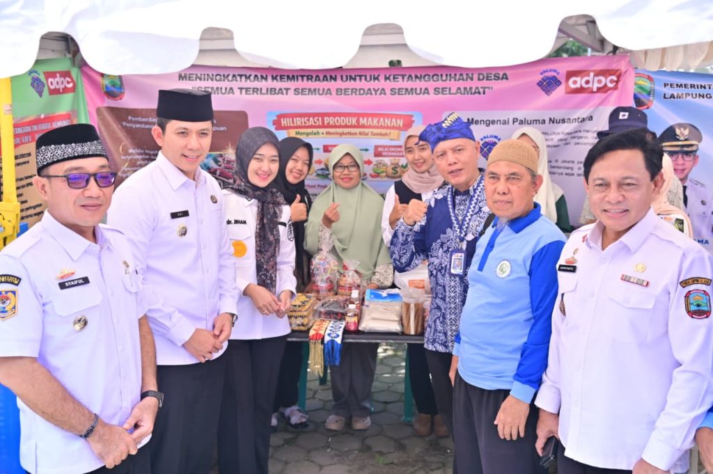 Pejabat pemerintah daerah dan tim komunitas berfoto bersama di stan pameran program pemberdayaan masyarakat yang menampilkan produk olahan lokal sebagai bagian dari upaya ketangguhan desa melalui hilirisasi produk pangan